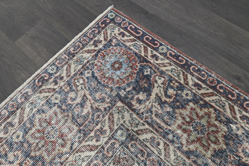 Pode incluir: Close-up de um canto de um tapete vintage com um padr&atilde;o azul, vermelho e creme. O tapete tem um design floral detalhado com detalhes intrincados.
