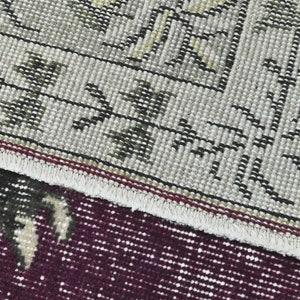 May include: Close-up of a rug with a detailed pattern of black and white lines and green leaves on a beige background. The rug has a red and white fringe border.