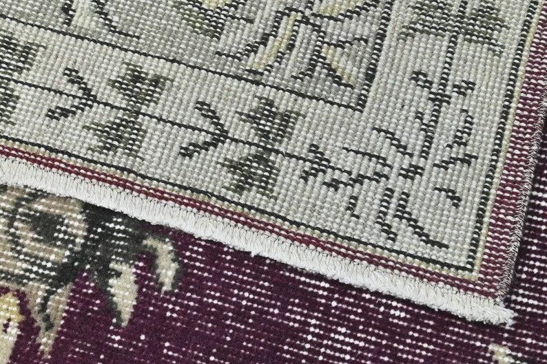 May include: Close-up of a rug with a detailed pattern of black and white lines and green leaves on a beige background. The rug has a red and white fringe border.