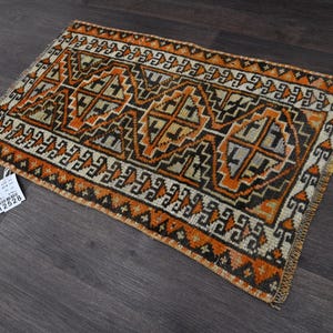 Puede incluir: Una alfombra rectangular con un patrón geométrico en tonos naranja, negro y crema. El diseño consiste en formas de diamante repetitivas y motivos de borde intrincados. Una pequeña etiqueta blanca con el número 12528 está unida a la esquina.
