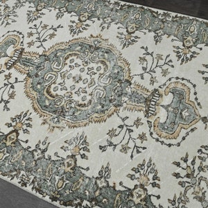 Op de afbeelding: Een vintage tapijt met een cr&egrave;mekleurige achtergrond en een gedetailleerd bloemenpatroon in tinten groen en bruin.
