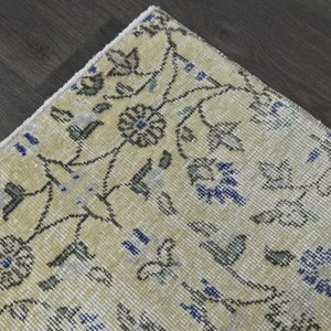 May include: A close-up of a cream-colored rug with a floral pattern in shades of blue, gray, and black. The rug has a fringe border.