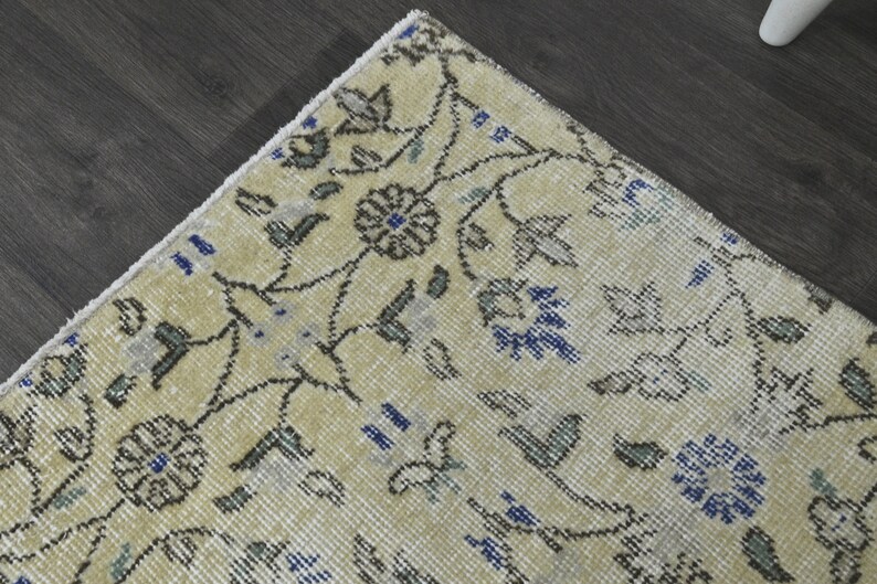 May include: A close-up of a cream-colored rug with a floral pattern in shades of blue, gray, and black. The rug has a fringe border.