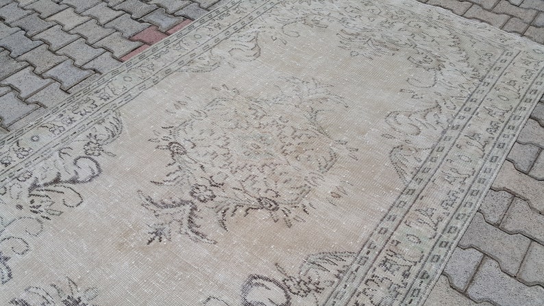 May include: A vintage rug with a faded floral pattern in shades of gray and white. The rug has a distressed look and is made of a soft, natural fiber.