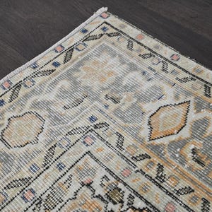 Puede incluir: Fragmento de una alfombra vintage con aspecto desgastado. La alfombra presenta una paleta de colores gris y crema con toques de naranja, rosa y azul. El dise&ntilde;o incluye patrones florales y geom&eacute;tricos, creando una est&eacute;tica tradicional.
