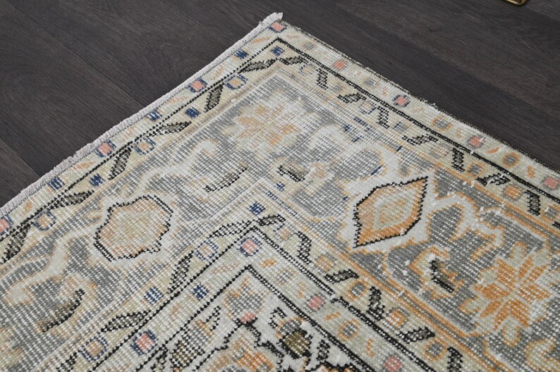 Puede incluir: Fragmento de una alfombra vintage con aspecto desgastado. La alfombra presenta una paleta de colores gris y crema con toques de naranja, rosa y azul. El dise&ntilde;o incluye patrones florales y geom&eacute;tricos, creando una est&eacute;tica tradicional.
