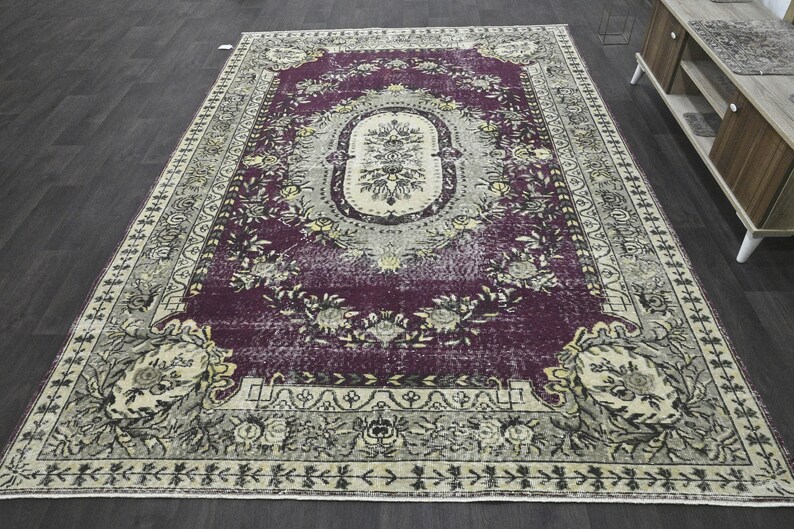 May include: A vintage-style rug with a faded purple background and intricate floral patterns in cream and beige. The rug has a distressed look and a worn border.