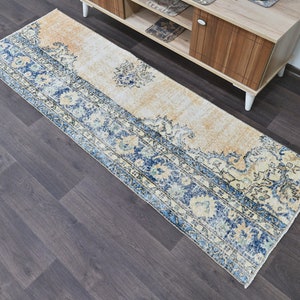 Op de afbeelding: Een vintage stijl loper met een cr&egrave;mekleurige achtergrond en een blauw bloemenpatroon. De loper heeft een verweerde look en is perfect om een ​​bohemien touch aan je huis toe te voegen.