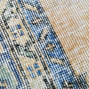 Op de afbeelding: Close-up van een geweven tapijt met een blauw, wit en beige patroon. Het tapijt heeft een textuur en een franje rand.