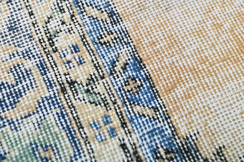 Op de afbeelding: Close-up van een geweven tapijt met een blauw, wit en beige patroon. Het tapijt heeft een textuur en een franje rand.