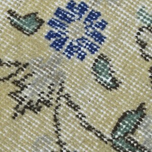 May include: Close-up of a beige rug with a repeating pattern of blue, green, and brown floral motifs. The rug has a textured surface.