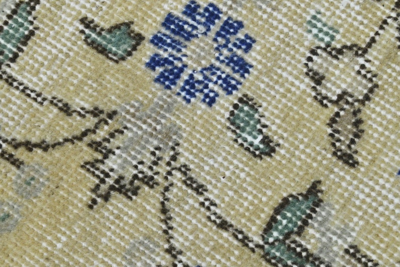 May include: Close-up of a beige rug with a repeating pattern of blue, green, and brown floral motifs. The rug has a textured surface.