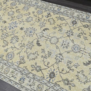 May include: A vintage rug with a cream background and a floral pattern in shades of gray and blue. The rug has a border with a repeating pattern.
