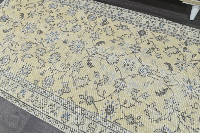 May include: A vintage rug with a cream background and a floral pattern in shades of gray and blue. The rug has a border with a repeating pattern.