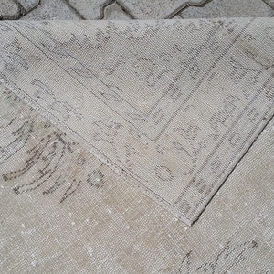 May include: A close-up of a light beige rug with a subtle pattern. The rug is folded in half, revealing the underside.