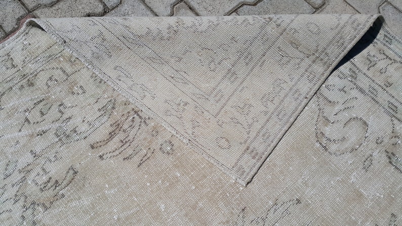 May include: A close-up of a light beige rug with a subtle pattern. The rug is folded in half, revealing the underside.