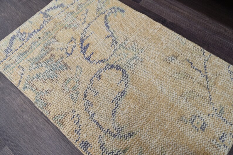 K&ouml;nnte beinhalten: Ein hellgelber Teppich mit einem blauen und gr&uuml;nen abstrakten Muster. Der Teppich hat eine gewebte Textur.