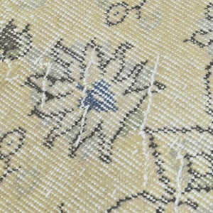 May include: Close-up of a beige rug with a floral pattern in shades of gray, white, and blue. The rug has a woven texture and a distressed look.