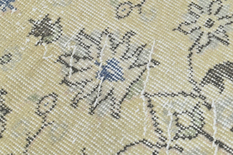 May include: Close-up of a beige rug with a floral pattern in shades of gray, white, and blue. The rug has a woven texture and a distressed look.