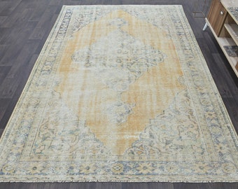 Puede incluir: Una alfombra vintage con un patrón descolorido en amarillo y azul. La alfombra tiene un aspecto desgastado y un borde con flecos.