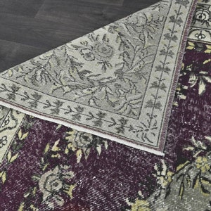 May include: A vintage rug with a floral pattern in shades of gray, white, and purple. The rug has a fringed edge and is made of wool.