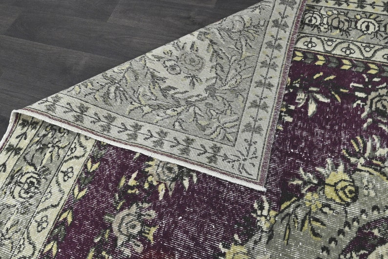May include: A vintage rug with a floral pattern in shades of gray, white, and purple. The rug has a fringed edge and is made of wool.