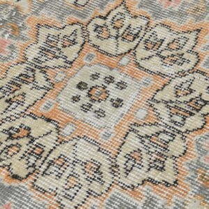 Puede incluir: Primer plano de una alfombra vintage con un dise&ntilde;o de medall&oacute;n central. La alfombra presenta una paleta de colores apagados de gris, beige y melocot&oacute;n, con intrincados patrones florales y geom&eacute;tricos. La textura de la alfombra parece suave y desgastada, lo que sugiere edad y uso.