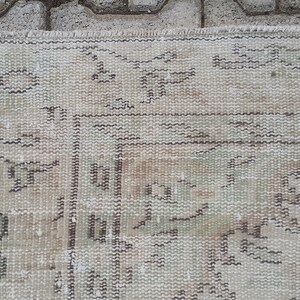 May include: A beige rug with a geometric pattern in brown and green. The rug is 63.5 inches by 101 inches, or 161 cm by 256 cm. The rug has a tag with the number 5002 on it.