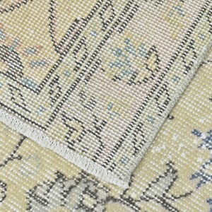May include: Close-up of a beige rug with a woven pattern. The rug has a fringe border and a subtle floral design in shades of blue and pink.