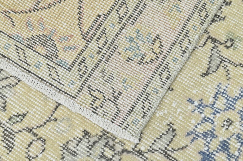 May include: Close-up of a beige rug with a woven pattern. The rug has a fringe border and a subtle floral design in shades of blue and pink.