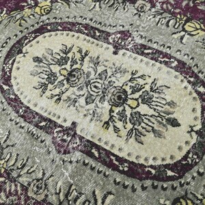 May include: A vintage rug with a floral pattern in shades of purple, gray, and yellow. The rug has a central oval medallion with a floral design.