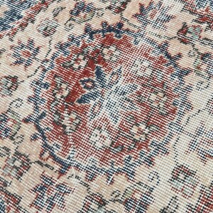 Pode incluir: Close-up de um tapete vintage com um padr&atilde;o detalhado em tons de azul, vermelho e creme.