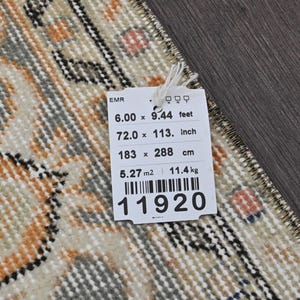 Puede incluir: Una alfombra rectangular con un dise&ntilde;o beige, naranja y gris. La alfombra mide 183 x 288 cm y 72,0 x 113 pulgadas. Una etiqueta adjunta a la alfombra muestra las dimensiones en pies, pulgadas, cent&iacute;metros y el peso de 11,4 kg.