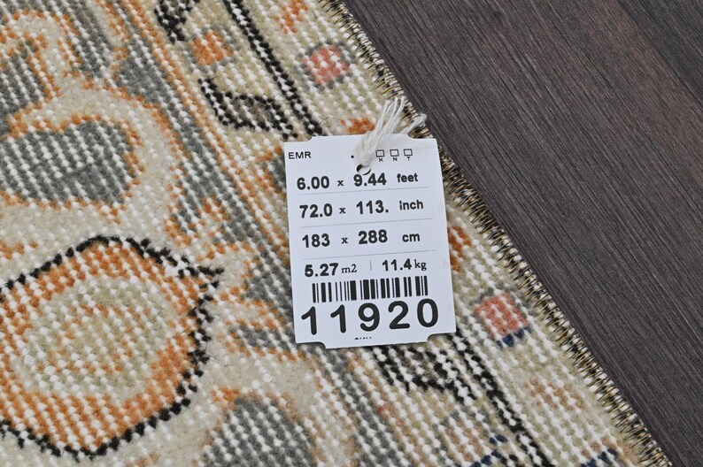 Puede incluir: Una alfombra rectangular con un dise&ntilde;o beige, naranja y gris. La alfombra mide 183 x 288 cm y 72,0 x 113 pulgadas. Una etiqueta adjunta a la alfombra muestra las dimensiones en pies, pulgadas, cent&iacute;metros y el peso de 11,4 kg.