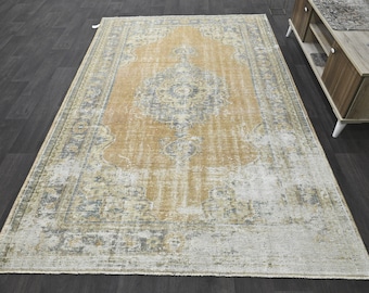 Puede incluir: Una alfombra de estilo vintage con un aspecto descolorido y desgastado. La alfombra tiene un fondo marrón claro con un patrón floral azul y blanco. La alfombra es rectangular y tiene un borde con flecos.