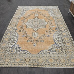 Puede incluir: Una alfombra de estilo antiguo con un dise&ntilde;o de medall&oacute;n central. La alfombra presenta un campo naranja c&aacute;lido con patrones florales y geom&eacute;tricos en azul, crema y gris. El borde tiene un patr&oacute;n floral detallado.