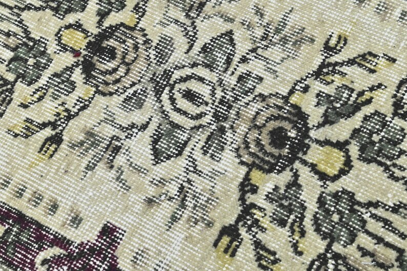 May include: Close-up of a beige rug with a floral pattern in shades of black, gray, and yellow. The rug has a distressed, vintage look.