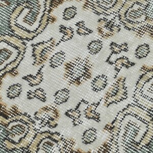 Op de afbeelding: Close-up van een tapijt met een patroon met een witte achtergrond en bruine en blauwe ontwerpen. Het tapijt heeft een geweven textuur.