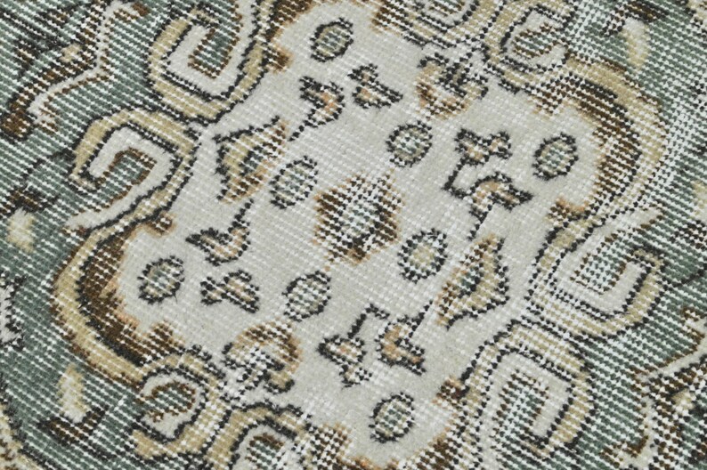 Op de afbeelding: Close-up van een tapijt met een patroon met een witte achtergrond en bruine en blauwe ontwerpen. Het tapijt heeft een geweven textuur.