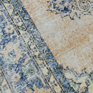 Op de afbeelding: Close-up van een beige kleed met een blauwe en witte bloemenrand. Het kleed heeft een verweerde, vintage uitstraling.