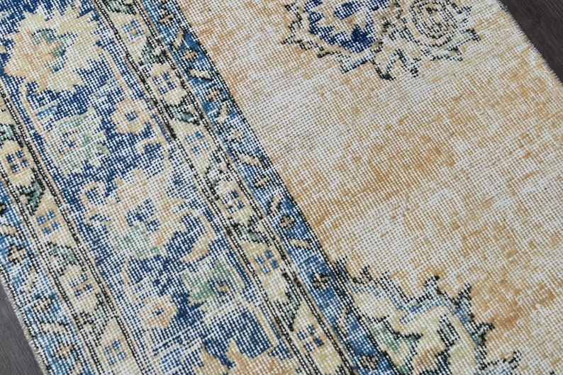 Op de afbeelding: Close-up van een beige kleed met een blauwe en witte bloemenrand. Het kleed heeft een verweerde, vintage uitstraling.