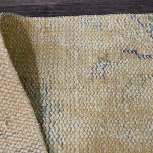 K&ouml;nnte beinhalten: Nahaufnahme eines beigefarbenen gewebten Teppichs mit einem dezenten Muster aus blauen und wei&szlig;en Linien. Der Teppich ist in der Mitte gefaltet und zeigt die Textur des Gewebes.