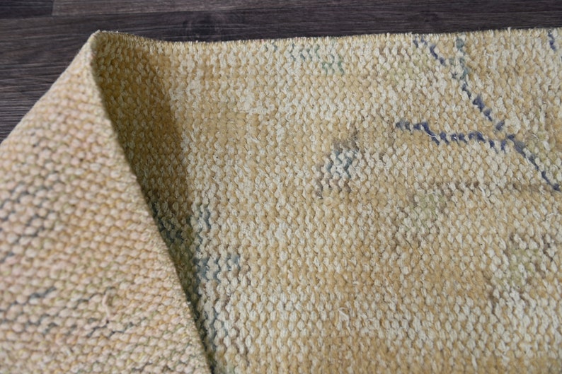K&ouml;nnte beinhalten: Nahaufnahme eines beigefarbenen gewebten Teppichs mit einem dezenten Muster aus blauen und wei&szlig;en Linien. Der Teppich ist in der Mitte gefaltet und zeigt die Textur des Gewebes.