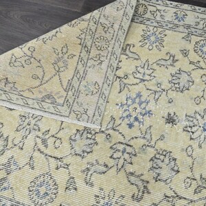 May include: A vintage rug with a cream background and a floral pattern in shades of blue and gray. The rug has a distressed look and is made of a soft, woven material.