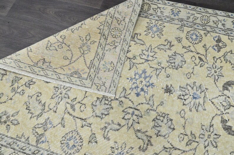 May include: A vintage rug with a cream background and a floral pattern in shades of blue and gray. The rug has a distressed look and is made of a soft, woven material.