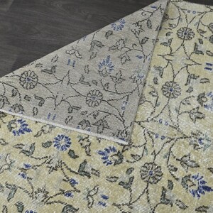 May include: A close-up of a beige rug with a floral pattern in shades of blue and gray. The rug has a subtle distressed look, giving it a vintage feel.