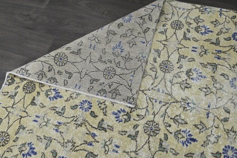 May include: A close-up of a beige rug with a floral pattern in shades of blue and gray. The rug has a subtle distressed look, giving it a vintage feel.