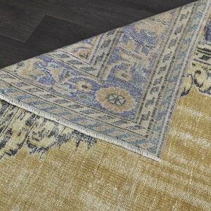 May include: A vintage rug with a faded yellow background and a blue and white geometric pattern. The rug has a frayed edge and a worn look.