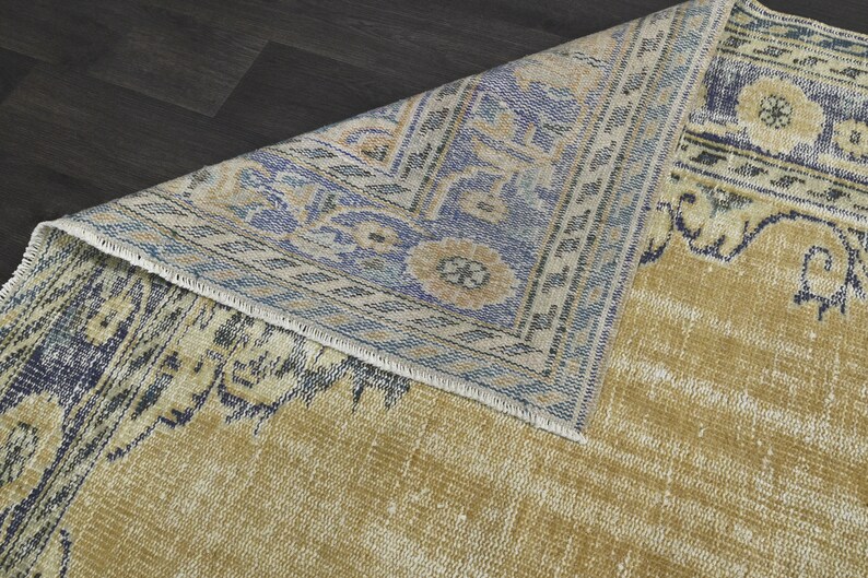 May include: A vintage rug with a faded yellow background and a blue and white geometric pattern. The rug has a frayed edge and a worn look.