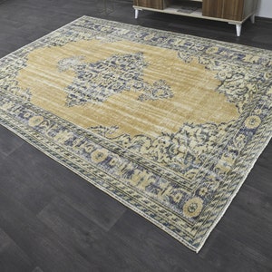 May include: A vintage-style rug with a beige background and a blue and white floral pattern. The rug has a distressed look and a fringed edge.